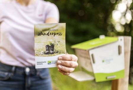 Eine Frau hält den Wanderpass vor den Stempelkasten