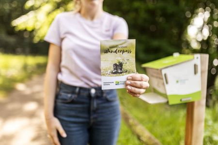 Eine Frau hält den Wanderpass vor den Stempelkasten