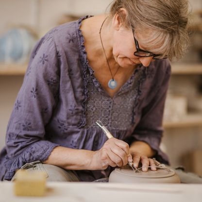Frau mit Brille töpfert an Töpferscheibe