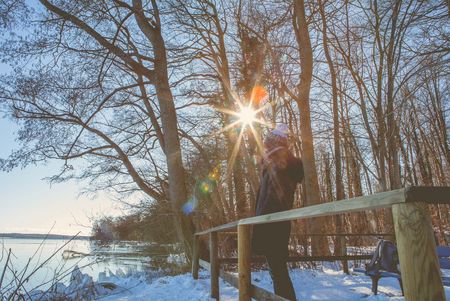 Person steht im Schnee vor Bäumen an einem Zaun