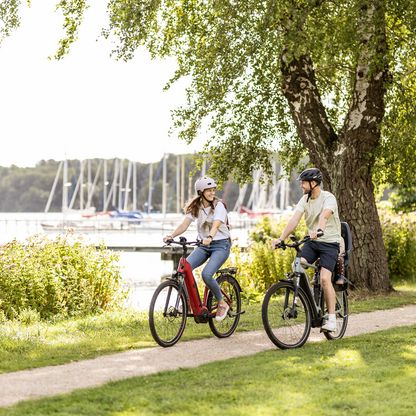 Zwei Personen fahren entlang des Sees auf einem Fahrradweg