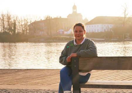 Die Mitarbeiterin der Eutin Tourismus GmbH Janett Paulauskas sitzt auf einer Bank an der Stadtbucht, im Hintergrund ist das Schloss Eutin zu sehen