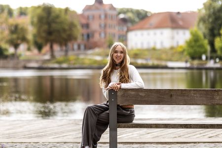 Jonna Engel sitzt auf einer Bank am Großen Eutiner See, im Hintergrund sieht man das Schloss Eutin.