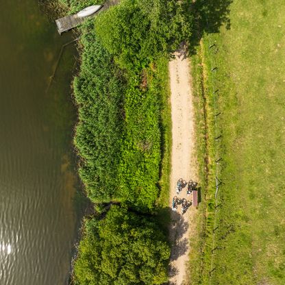 Ein Radweg aus der Vogelperspektive mit Radfahrern und dem See